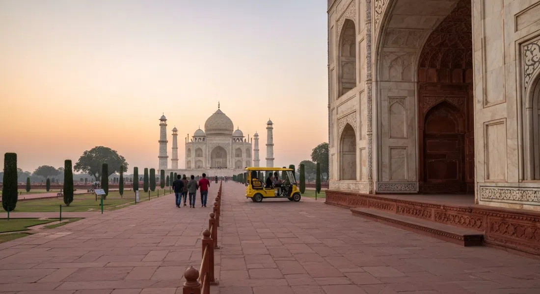 el acceso por la Puerta Este al Taj Mahal al amanecer, con un camino peatonal tranquilo, un buggy eléctrico gratuito a lo lejos y el mármol brillando tenuemente al frente