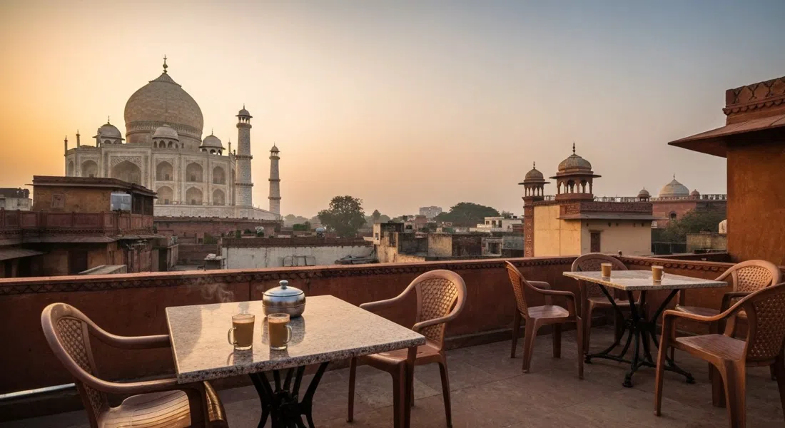 una terraza en azotea en Taj Ganj con la cúpula del Taj Mahal visible sobre los techos bajos al amanecer, vasos de chai y sillas de plástico en primer plano